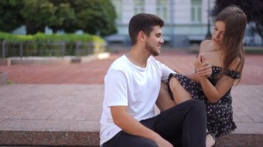 Loving happy young couple sitting on curb holding hands smiling enjoying date. portrait of beautiful Caucasian woman and handsome bearded man dating in city on street