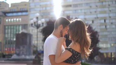 Side view zoom in to happy hugging couple talking standing on city street. Smiling Caucasian millennial boyfriend and girlfriend embracing in sunbeam outdoors in slow motion