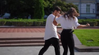 Tracking shot of young man holding hand of woman riding skateboard on city street smiling. Happy carefree Caucasian girlfriend having fun dating with loving boyfriend outdoors at sunset. Slow motion