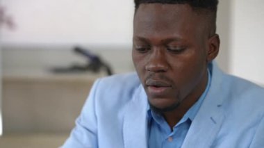 Yakın plan Afro-Amerikan, mavi takımlı genç adam ofiste çalışıyor ve çay içiyor. Zeki, odaklanmış iş adamı planlama fikri sıcak içecekle ferahlatıcı.