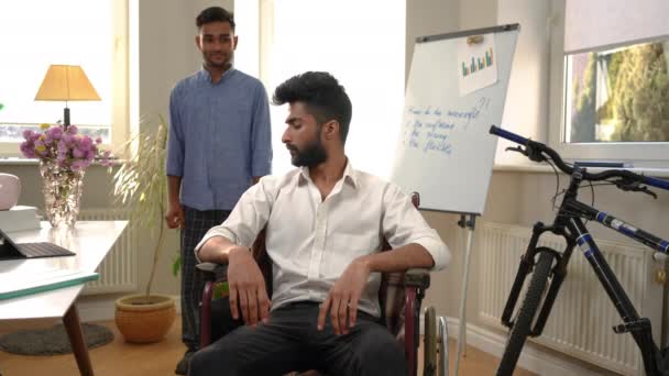 車椅子で幸せな若い中東の男の友人を振り返り カメラの笑顔を見て 同僚と自宅のオフィスでポーズ正の自信の100万人のスタータの肖像 — ストック動画