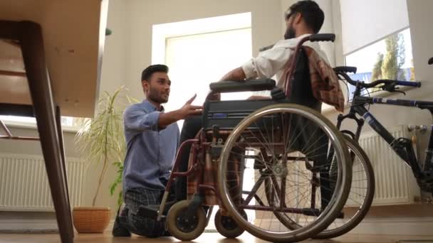 一个支持他的年轻人跪下来 牵着坐在轮椅上的悲伤朋友的手 一边说一边笑着 中东男人在意外中支持心烦意乱的伴侣的全景画像 — 图库视频影像