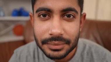 Close-up face of bearded young Middle Eastern man with mustache black hair and brown eyes looking at camera. Smiling confident handsome guy posing indoors