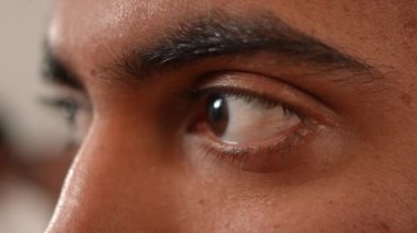 Yakın plan erkek kahverengi göz başka tarafa bakıyor ve etrafına bakıyor. Kapalı alanda siyah saçlı Orta Doğulu genç adamın aşırı yakın plan yüzü.