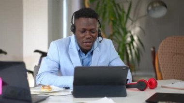Çevrimiçi tablette web sohbeti kullanarak el sallayan pozitif genç serbest yazar. Yakışıklı Afro-Amerikan adam ofisten internetten gülümsüyor.