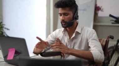 Teknik ekip kulaklıklarda profesyonelce dizüstü bilgisayarla konuşuyor. İçerideki ofiste oturuyor. Tekerlekli sandalyede çalışan yakışıklı Orta Doğulu bir adamın portresi.