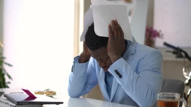 疲惫不堪的年轻人手牵着头坐在屋里的桌子旁 手里拿着文书工作 身穿蓝色西装的非裔美国商人一边叹息一边想 — 图库视频影像