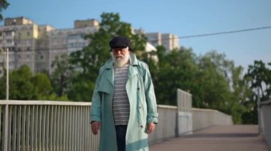 Portrait of old bearded Caucasian man with gray hair walking in slow motion in city leaving. Senior male retiree strolling outdoors on sunny summer spring day. Lifestyle concept