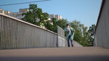 Wide shot cheerful senior bearded man dancing in slow motion on urban city bridge on sunny spring summer day. Portrait of joyful happy relaxed Caucasian retiree having fun outdoors