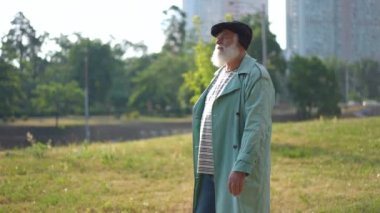 Tracking shot side view of senior confident man strolling in slow motion walking upstairs to urban bridge leaving. Handsome Caucasian bearded gray-haired male retiree enjoying sunny day in town