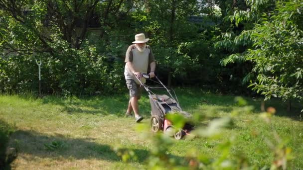 在春夏的室外花园 头戴草帽的老人推着割草机散步 白种人自信的园艺者慢动作在草地上修剪草坪的全景画像 — 图库视频影像