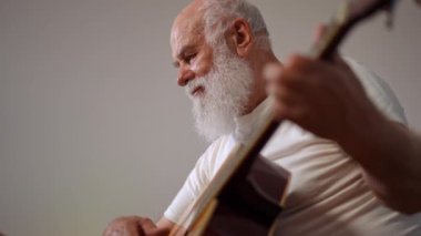 Bottom angle view portrait of inspired senior guitarist writing song touching strings in slow motion thinking. Happy confident Caucasian musician enjoying hobby and lifestyle at home indoors