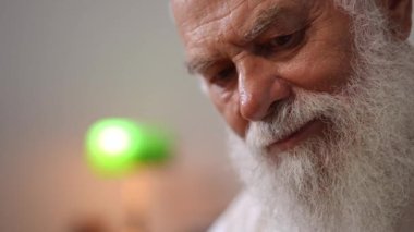 Headshot of curios concentrated old man with gray beard and mustache looking down and around sitting indoors. Happy relaxed confident Caucasian retiree enjoying leisure at home