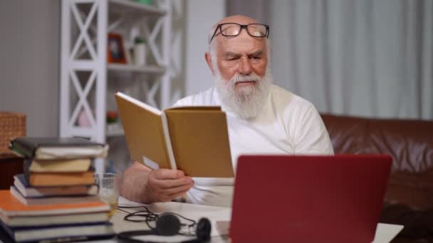 Koncentrerad Senior Man Läser Bok Meddelanden Online Laptop Leende Porträtt — Stockvideo