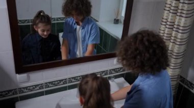 High angle view two cheerful kids brushing teeth in bathroom in front of mirror. Happy joyful Caucasian brother and sister getting ready for school in the morning at home