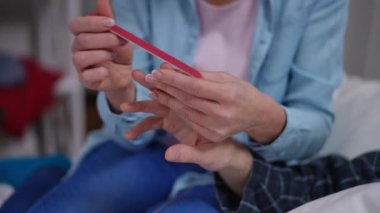 Close-up female hands filing male nails sitting on bed in bedroom. Unrecognizable Caucasian wife taking care of ill husband at home indoors. Pampering and relationship concept