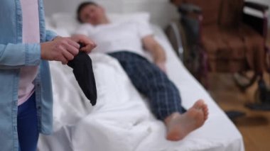 Tanımlanamayan kadın evde yatan bulanık ayaklı adam için çorap hazırlıyor. Hasta kocayı yatak odasında giydirmeye bayılan beyaz bir eş. Ev hayatı ve bakım konsepti