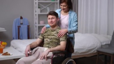 Beautiful woman walking to handsome man in wheelchair hugging spouse posing. Positive loving Caucasian husband and wife looking at camera smiling. Relationship and support concept