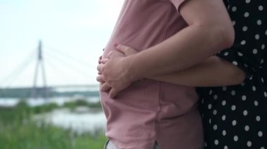 Side view unrecognizable young woman caressing pregnant belly of man standing outdoors. Female hand stroking Caucasian male abdomen at background of spring summer landscape. Fun concept