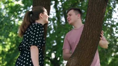 Smiling loving man standing in sunny park with pregnant woman talking touching face of spouse. Portrait of happy Caucasian husband enjoying leisure with wife outdoors on spring summer day