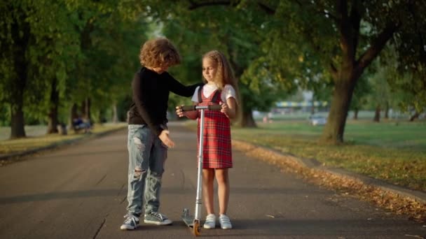 广泛拍摄的白人男孩说话的女孩教骑踏板车 好奇的孩子在好朋友的支持下学习骑车 — 图库视频影像