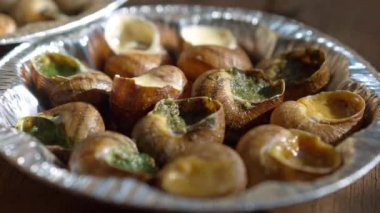 Extreme close-up plate with cooked escargot in sunlight outdoors. Closeup delicious exotic food on wooden table