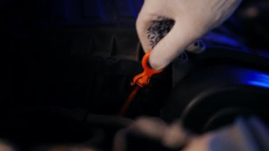 Close-up male hands in gloves pulling out dipstick checking engine oil level. Unrecognizable Caucasian auto mechanic at service station indoors with vehicle