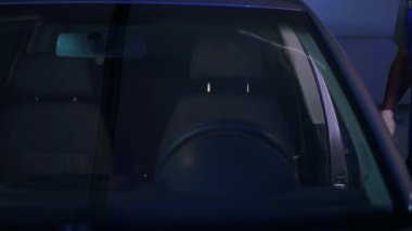 Young confident auto mechanic opening car door sitting down on drivers seat starting engine. Front view concentrated Caucasian tattooed man checking vehicle after maintenance