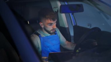 Sürücü koltuğunda oturan oto tamircisi araçtaki yazılım arızalarını kontrol ediyor. Kafkasyalı genç bir adamın otomobilde tamir sorunu portresi. Ön camdan ateş ediyorlar.