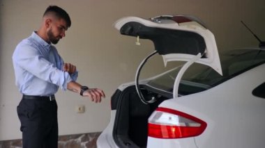 Car with open trunk and flashing backlit in garage with young man rolling up sleeves taking liquid tank. Side view Caucasian driver with automobile indoors