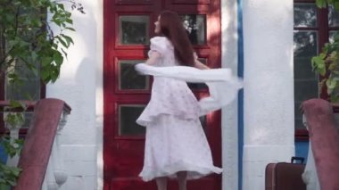 Joyful confident retro lady spinning on porch smiling looking away. Portrait of attractive elegant gorgeous Caucasian redhead woman in vintage dress having fun outdoors