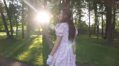 Confident elegant lady in vintage dress smiling strolling in sunshine in park. Happy beautiful slim Caucasian young woman in retro outfit walking outdoors looking around