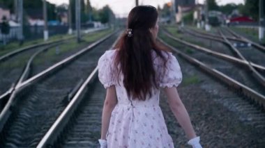 Eski moda elbiseli, antika bavullu, güvenilmez genç bir kadın demiryolunda yürüyor ve etrafa bakıyor. Beyaz tenli güzel bir kadının zaman yolculuğu yaparken çekilmiş bir portresini izliyorum. KostümComment