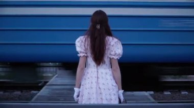 Back view woman in retro dress standing outdoors with train passing fast. Medium shot young slim Caucasian lady in vintage outfit outdoors