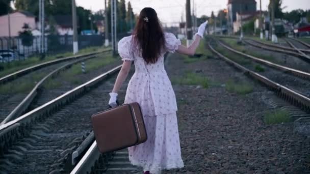 전통적 가방을 철길을 밖에서 산책하는 여성의 백라이트 — 비디오