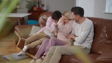 Neşeli oğul ve koca evdeki oturma odasında oturan gülen kadını gıdıklıyor. Olumlu neşe saçan beyaz erkek ve kadın hafta sonları evde eğleniyorlar.