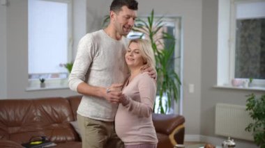 Evde hamile bir kadınla dans eden mutlu kocayı sevmek. Gülümseyen beyaz adam, kadınlara sarılıyor ve eğleniyor. Birliktelik ve aile kavramı