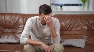 Oturma odasında kanepede oturan sorunlu beyaz yakışıklı adamın portresi. Evde yalnız başına üzgün, düşünceli bir adamın orta ölçekli görüntüsü.