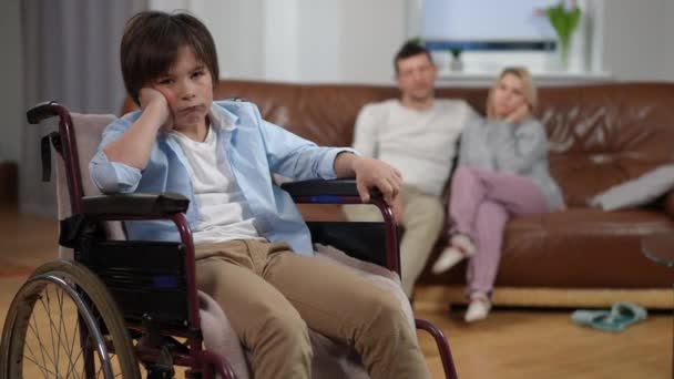 Tekerlekli Sandalyedeki Üzgün Çocuğun Kameraya Bakıp Koltukta Oturan Bulanık Erkek — Stok video