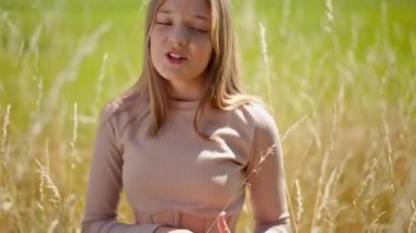 Güneşin altında buğday tarlasında kameraya bakarak şarkı söyleyen güzel esmer kız. Açık havada poz veren yetenekli kendine güvenen genç şarkıcının ön manzara portresi. Doğa ve sanat konsepti