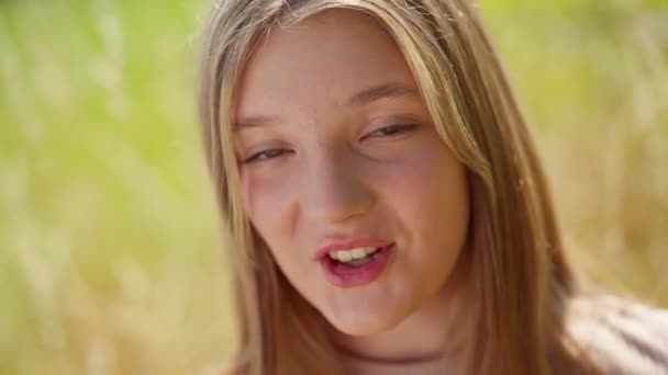 クローズアップブルネットティーンの女の子と茶色の目が屋外でポーズをとって笑顔を歌っています 幸せな熟練した白人の10代の歌手の肖像 太陽の下でフィールド上で実行されるカメラを見て — ストック動画