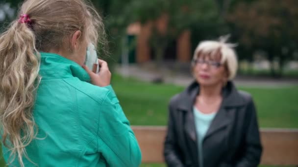 拍拍才华横溢的女孩的肩头 在户外给年长的模糊的女人拍照 好奇的白种人孙女在公园里享受着与祖母共度时光的乐趣 — 图库视频影像