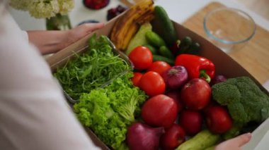 Meyve ve sebze kutuları yerleştiren tanınmayan bir kadınla dolu bir masa. Salata malzemelerini seçen beyaz bir bayanın omzunun üstünden ateş ediyor.