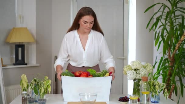 Jovem Mulher Confiante Trazendo Caixa Com Frutas Legumes Para Mesa — Vídeo de Stock
