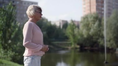 Green Tree Gölü ve Çeşmesi 'nin solunda duran kendinden emin yaşlı kadın. İnce, beyaz saçlı, beyaz bir bayan şehir parkında eğleniyor.