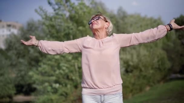 兴奋的高个子白人女人伸出手来 看着外面阳光灿烂的天气 夏春公园中景照片 自信满意的退休人士 — 图库视频影像