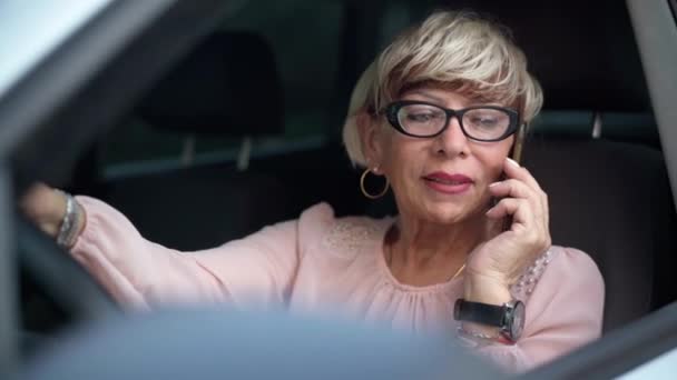 老年妇女坐在汽车司机座位上电话交谈的肖像 自信漂亮的白种人退休女性在户外的车里用智能手机聊天 — 图库视频影像