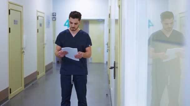 Koncentrerad Intelligent Manlig Läkare Undersöker Sjukdomshistoria Stående Sjukhuskorridoren Inomhus Porträtt — Stockvideo