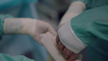 Yakın plan hemşire, cerrahın yavaş çekimde steril tıbbi eldiven giymesine yardım ediyor. Tanımlanamayan kadın ve erkek klinikteki ameliyathanede ameliyata hazırlanıyorlar.