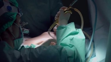 Hemşirenin omzunun üstünden çekerek cerrahın ensizyonu yavaş çekimde temizlemesine yardımcı oluyor. Ameliyathanede profesyonel bir erkeğe asistanlık yapan bir kadın. Tıp konsepti